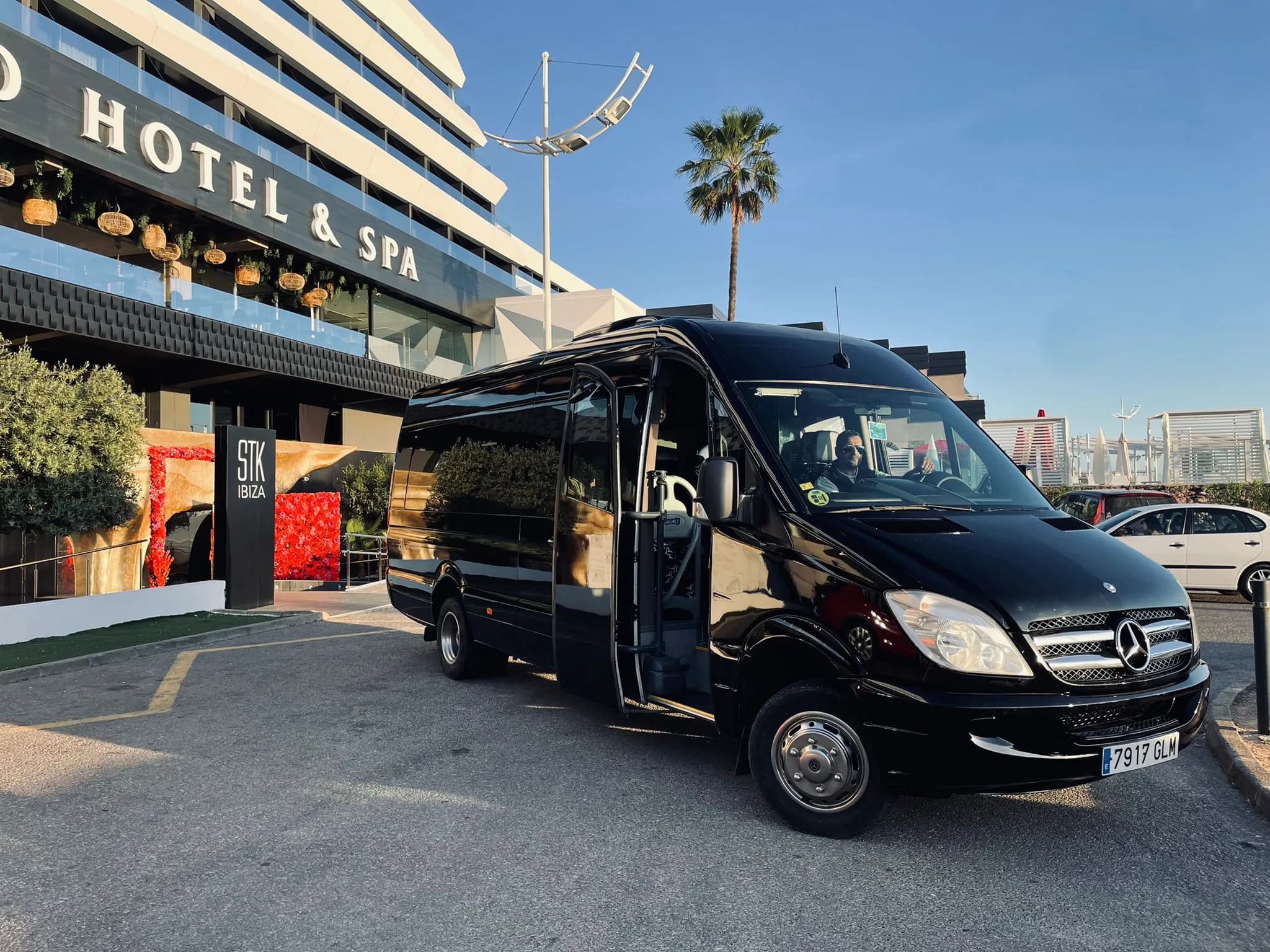 A black Mercedes Sprinter waiting outside a hotel in Ibiza with the driver at the wheel