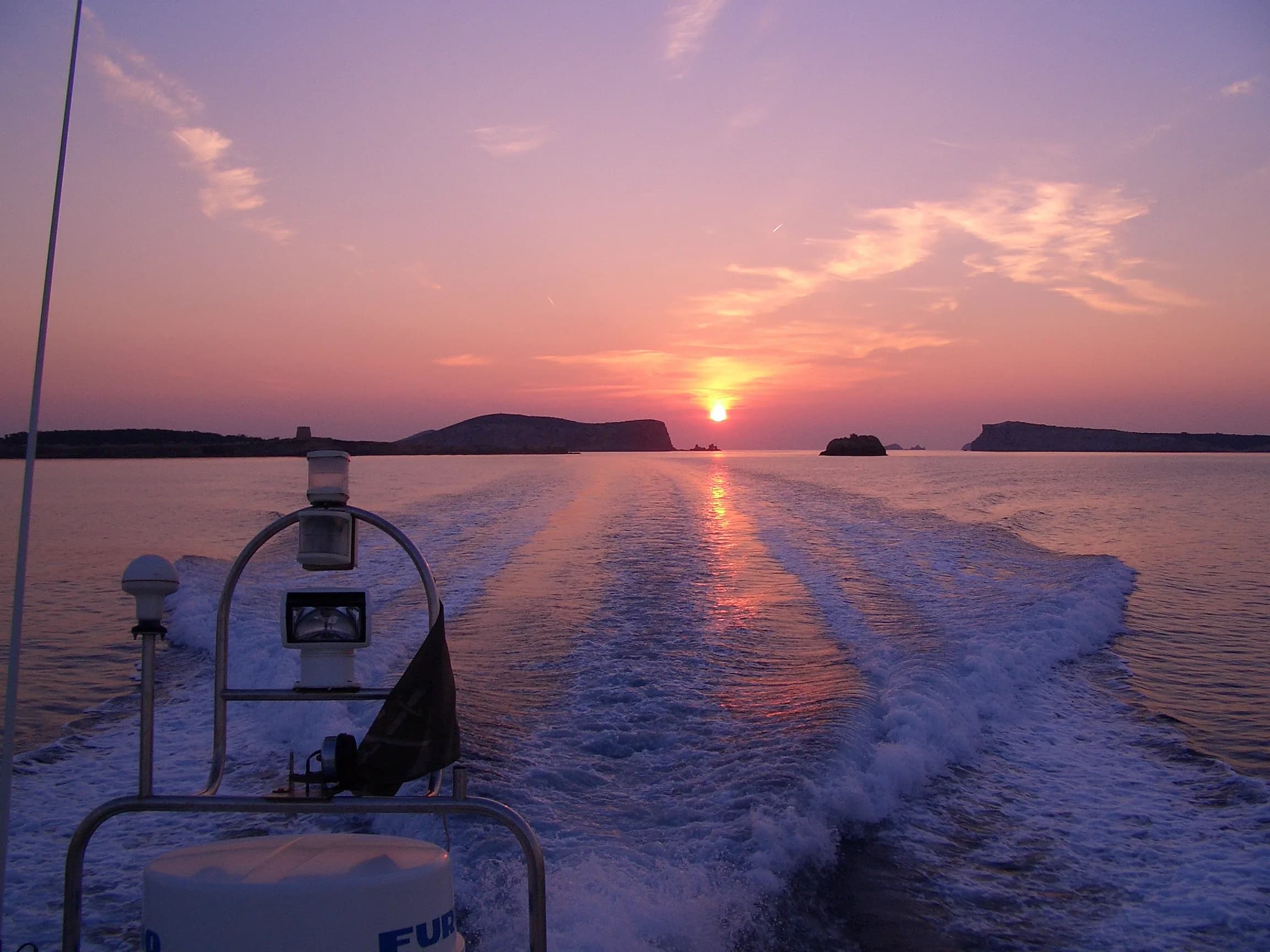 The wake of a boat heading back past the islands as the sun sets off Ibiza